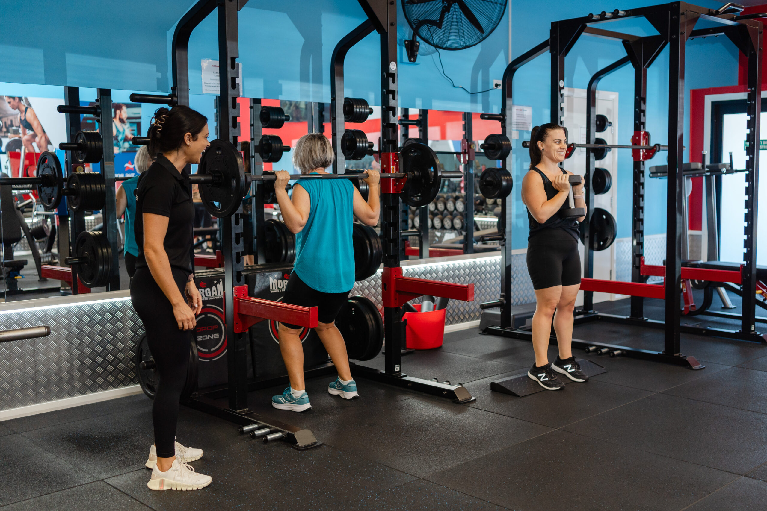 A trainer supervises two women during a leg workout at a gym