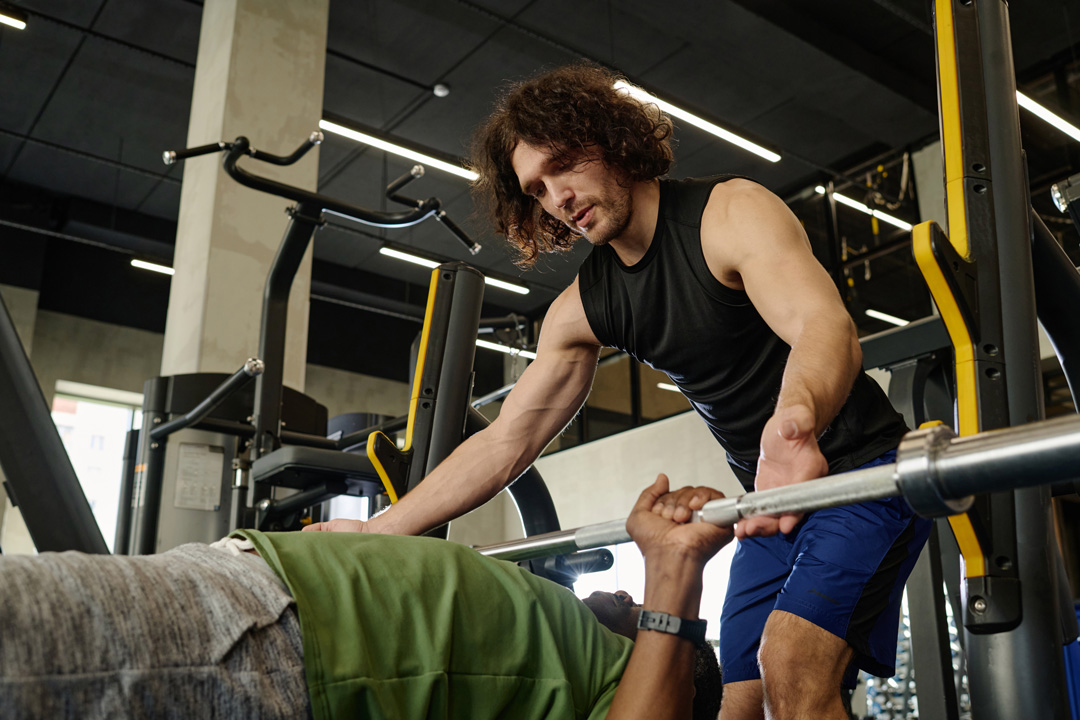 Personal trainer spotting a man during bench press at a gym.