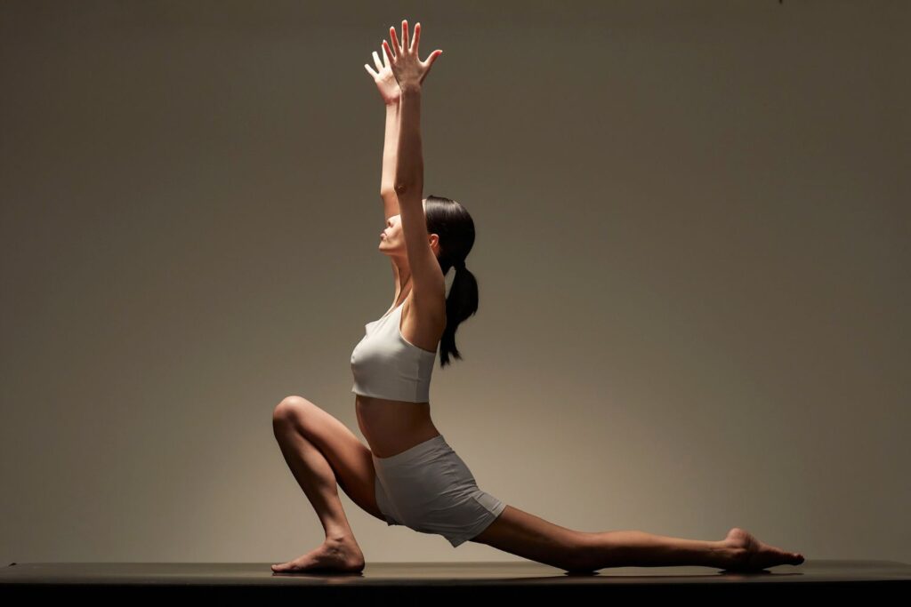 A woman in a white athletic top and shorts performs a low lunge yoga pose