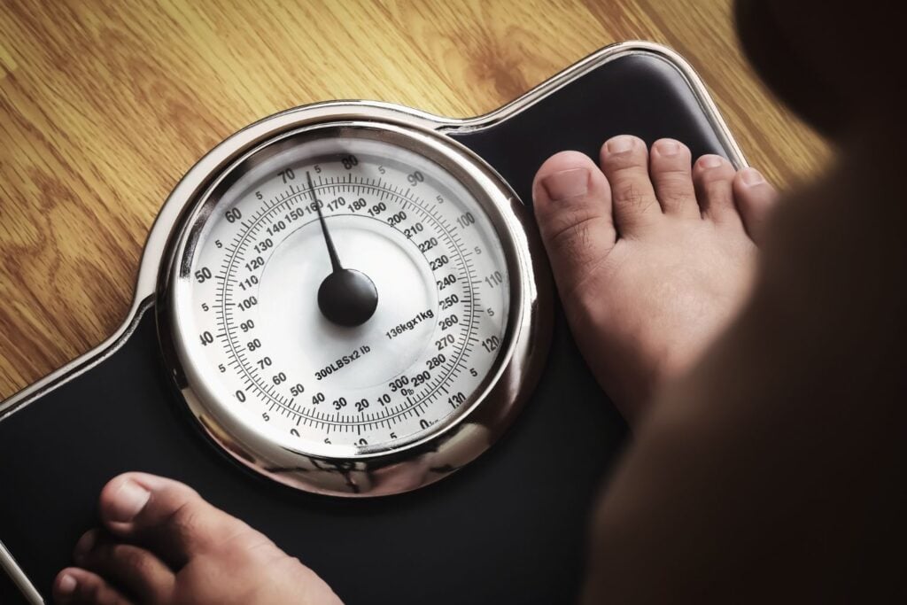 a person's feet as they stand on an analog bathroom scale, which indicates a weight of approximately 163 pounds.