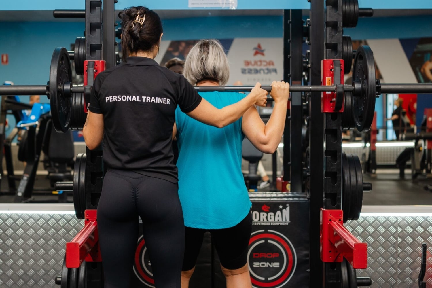 Female personal trainer assisting a client with barbell squats at Active Fitness Medowie