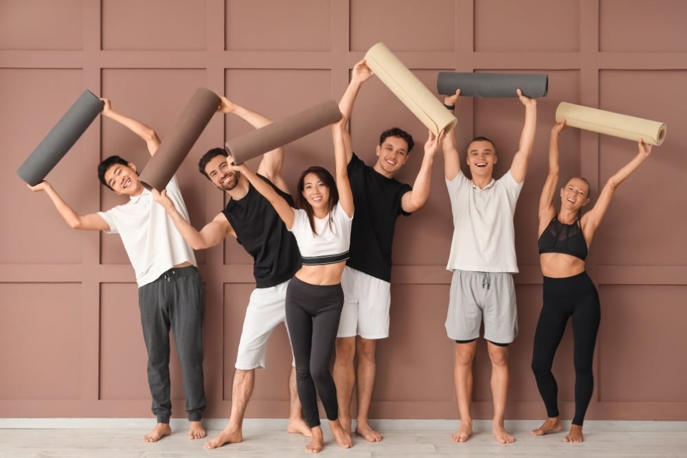 Six friends holding yoga mats overhead in studio