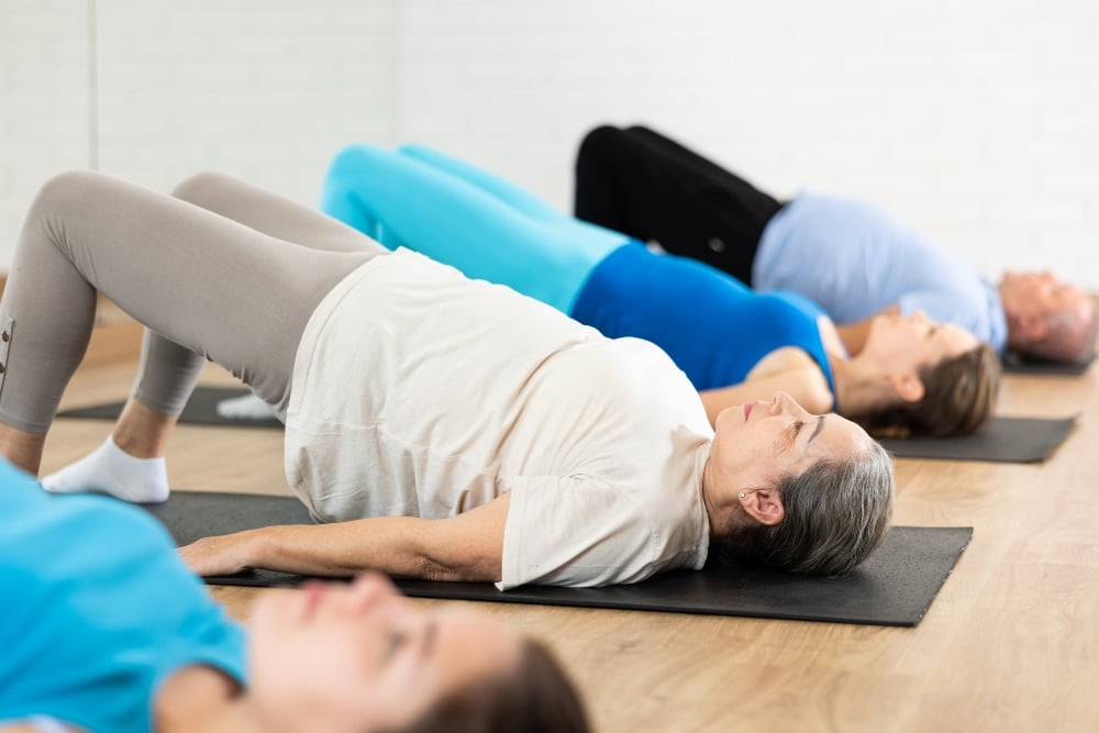 A group of people in an exercise class lying on yoga mats while performing a glute bridge pose.