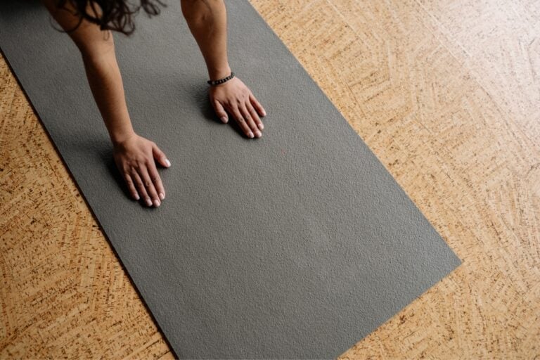 An overhead view of a person's hands firmly planted on a grey mat for a zen mat pilates class.