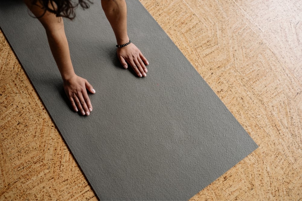 An overhead view of a person's hands firmly planted on a grey mat for a zen mat pilates class.