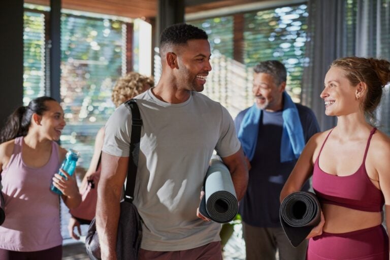 Group of smiling people holding yoga mats chatting before or after a workout class.