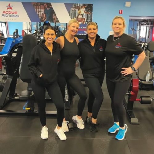 Four women in black athletic wear pose together for a group photo in a gym at Active Fitness Medowie, surrounded by various weight machines.