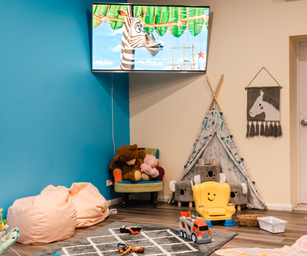 A vibrant children's playroom featuring a blue accent wall and a wall-mounted TV playing the movie Madagascar.
